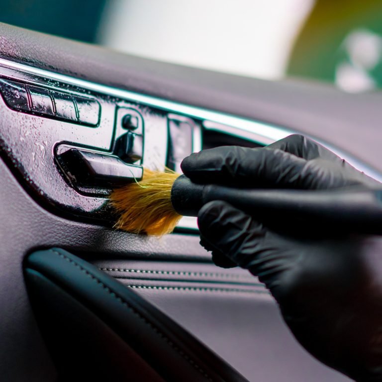 Car wash worker thoroughly cleaning the interior of a luxury car with a brush detailing close-up